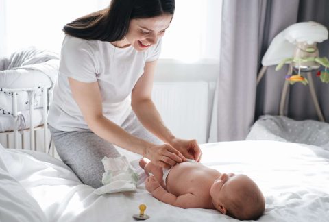 Mother and baby boy communicating after sleep. Caucasian child changing diaper at home. Adorable smiling family play together. Authentic candid lifestyle domestic moments.