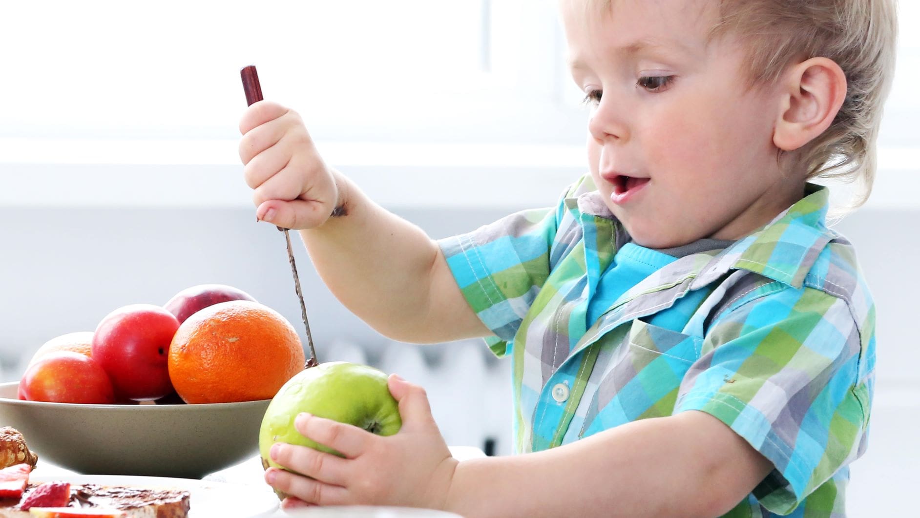 niño se esfueza por pelar una fruta sin ayuda de los adultos